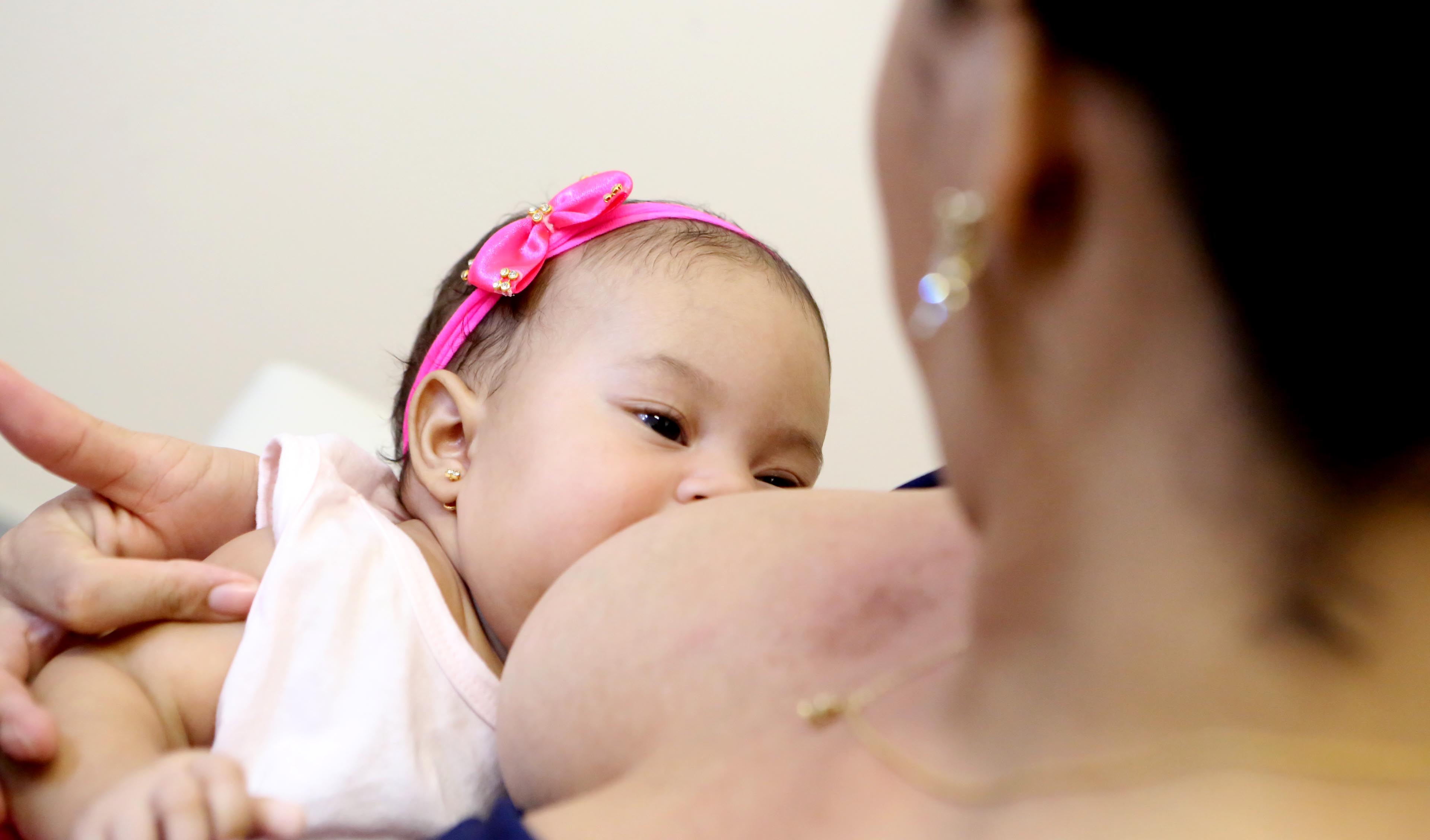 Mãe amamentando filha bebê com laço na cabeça